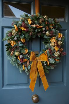 a christmas wreath hanging on a blue door with gold ribbon and bells attached to it