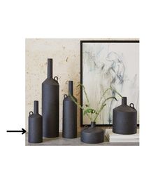 three black vases sitting on top of a table next to a framed art piece