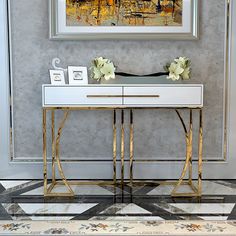 a white and gold console table in front of a wall with a painting on it