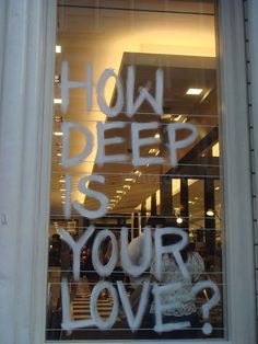 graffiti written on the window of a store front that says how deep is your love?