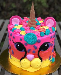 a cake decorated with pink, yellow and blue frosting has a cat's face on it