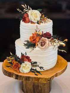 a three tiered white cake with orange and red flowers on top sits on a wooden stand