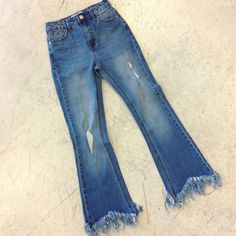 a pair of blue jeans with holes and fraying on the bottom, sitting on a white surface