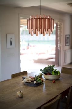 a wooden table topped with a bowl of vegetables and a light fixture hanging from the ceiling