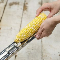 a person using a knife to cut corn on the cob