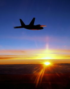 an airplane flying in the sky at sunset with the sun setting behind it and some clouds