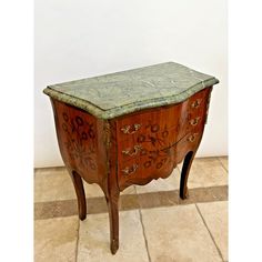 an old wooden table with green marble top and drawers on the bottom, sitting on tile flooring