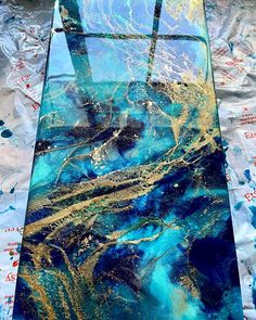 an artistic glass table with blue and gold paint on it, sitting on top of foil