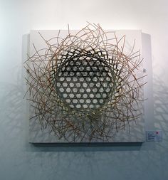 a sculpture made out of sticks on top of a white board with holes in the middle