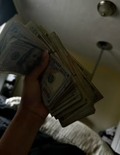 a person holding money in their hand on top of a bed with a ceiling fan