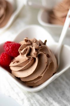 a bowl filled with chocolate frosting and raspberries on top of a table