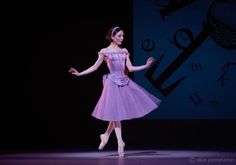 a woman in a purple dress is performing on stage with her arms outstretched and legs spread out