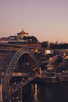 a bridge that is over some water with buildings in the background and lights on it