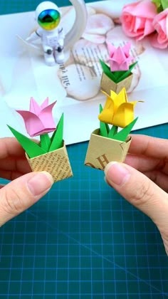 two hands holding origami flowers in front of a piece of paper