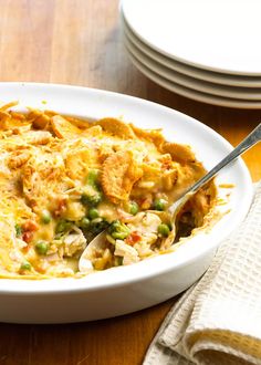 a white bowl filled with chicken and vegetable casserole on top of a wooden table