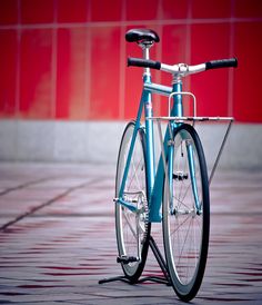 a blue bicycle parked on the side of a road next to a red wall and floor