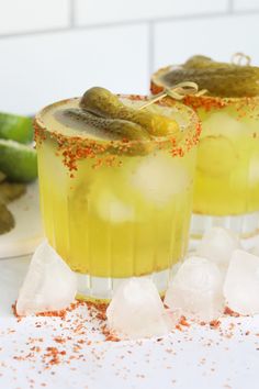 two glasses filled with lemonade and cucumber garnish on top of ice