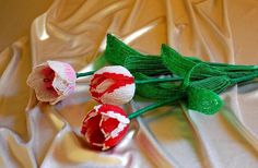 three red and white flowers sitting on top of a cloth covered table next to each other