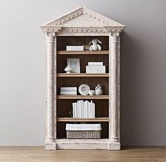 an old bookcase with books and other items on it in front of a gray wall