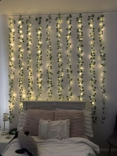 a bed with white sheets and lights on the wall above it is decorated with ivy vines