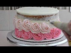 someone is decorating a cake with pink and white frosting on the top tier