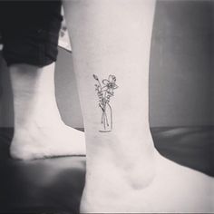 a woman's foot with a small flower vase tattoo on the left side of her leg