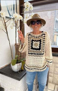 an older woman standing in front of a window wearing a crocheted sweater and hat