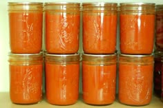 several jars filled with orange colored liquid on top of a wooden table next to other jars