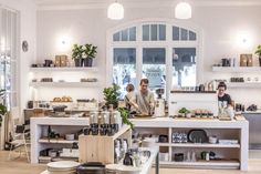 two men working behind the counter in a restaurant with lots of food on it and plants