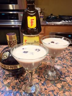 two glasses filled with liquid sitting on top of a counter next to a bottle of booze