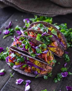 three tacos filled with vegetables on top of a wooden table