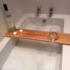 a bath tub with a wine glass and bottle on the edge that says relax in cursive writing