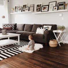 a baby sitting on the floor in front of a couch and coffee table with pictures above it