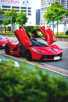 two red sports cars parked next to each other on the side of a road in front of tall buildings