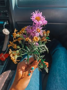 a person holding flowers in their hand while sitting in the driver's seat of a car