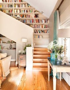 a living room filled with lots of furniture and bookshelves next to a stair case