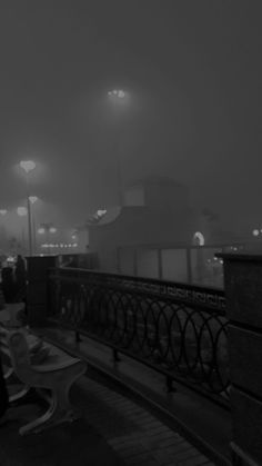 people are sitting on benches in the fog at night, with street lights above them