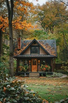 a small house in the woods surrounded by trees with fall leaves on it's roof