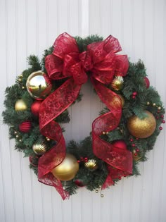 a christmas wreath with red ribbon and ornaments hanging on the front door ornament