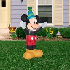 a mickey mouse inflatable balloon sitting on the grass with his hands up and smiling