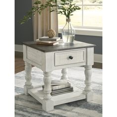 a white end table sitting on top of a rug next to a vase filled with flowers