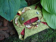 a green bag sitting on the ground next to a leafy plant and some leaves