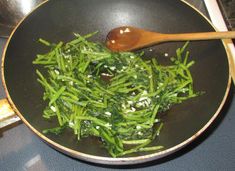 green beans and spinach are being cooked in a frying pan with a wooden spoon