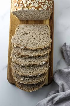 sliced oatmeal bread on a wooden cutting board next to a gray towel