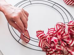 a person is decorating a wreath with red and white ribbons on it while another hand holds the ribbon