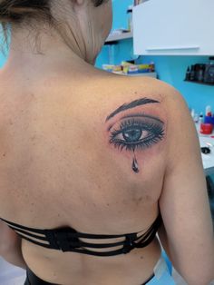 a woman with a tattoo on her back has an eye and tear coming out of it