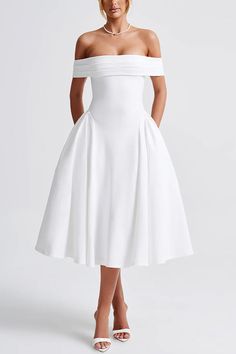 a woman wearing a white dress with off the shoulder sleeves and high low heels standing in front of a white background