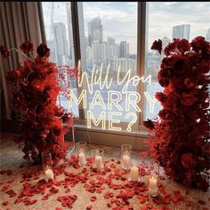 red flowers and candles sit in front of a window with the words will you marry me?