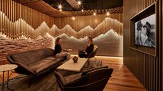 two women sitting on couches in front of a wall with wooden slats behind them