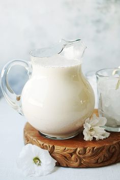 a pitcher of milk sitting on top of a wooden table next to two glasses filled with liquid